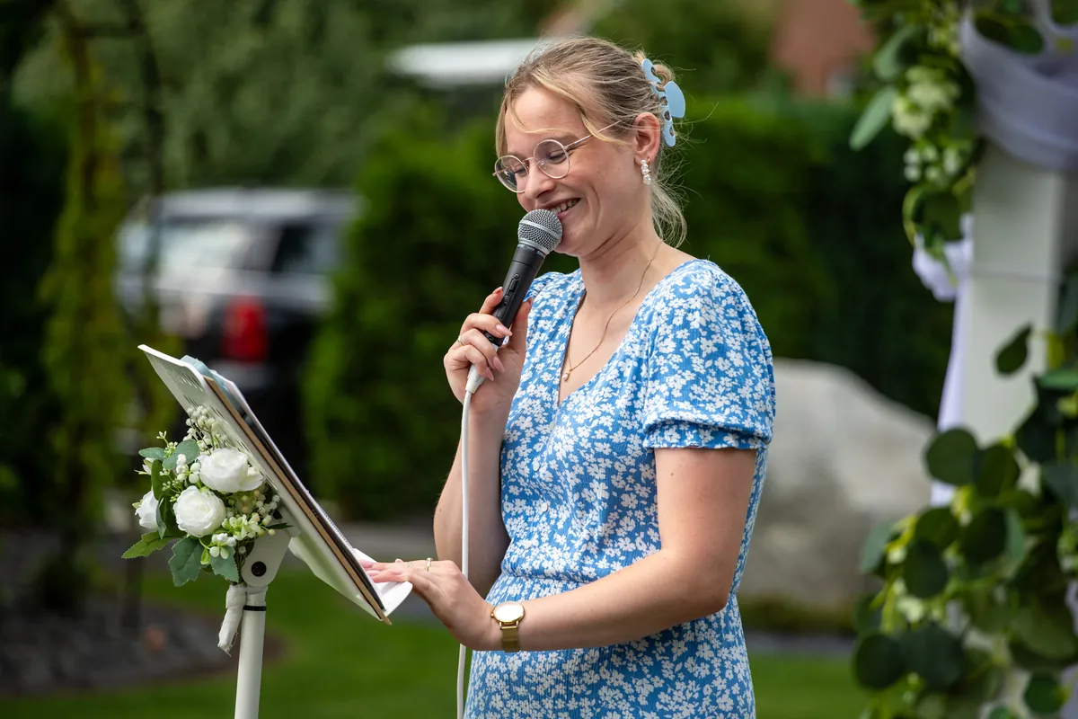 Freie Rednerin Emma Angermann hält mit Mikrofon eine Rede bei einer freien Trauung im Grünen